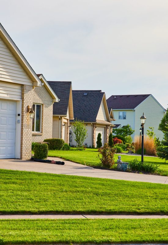 Image of Row of brick-faced houses, green manicured lawns, summer trees, gray blue sky